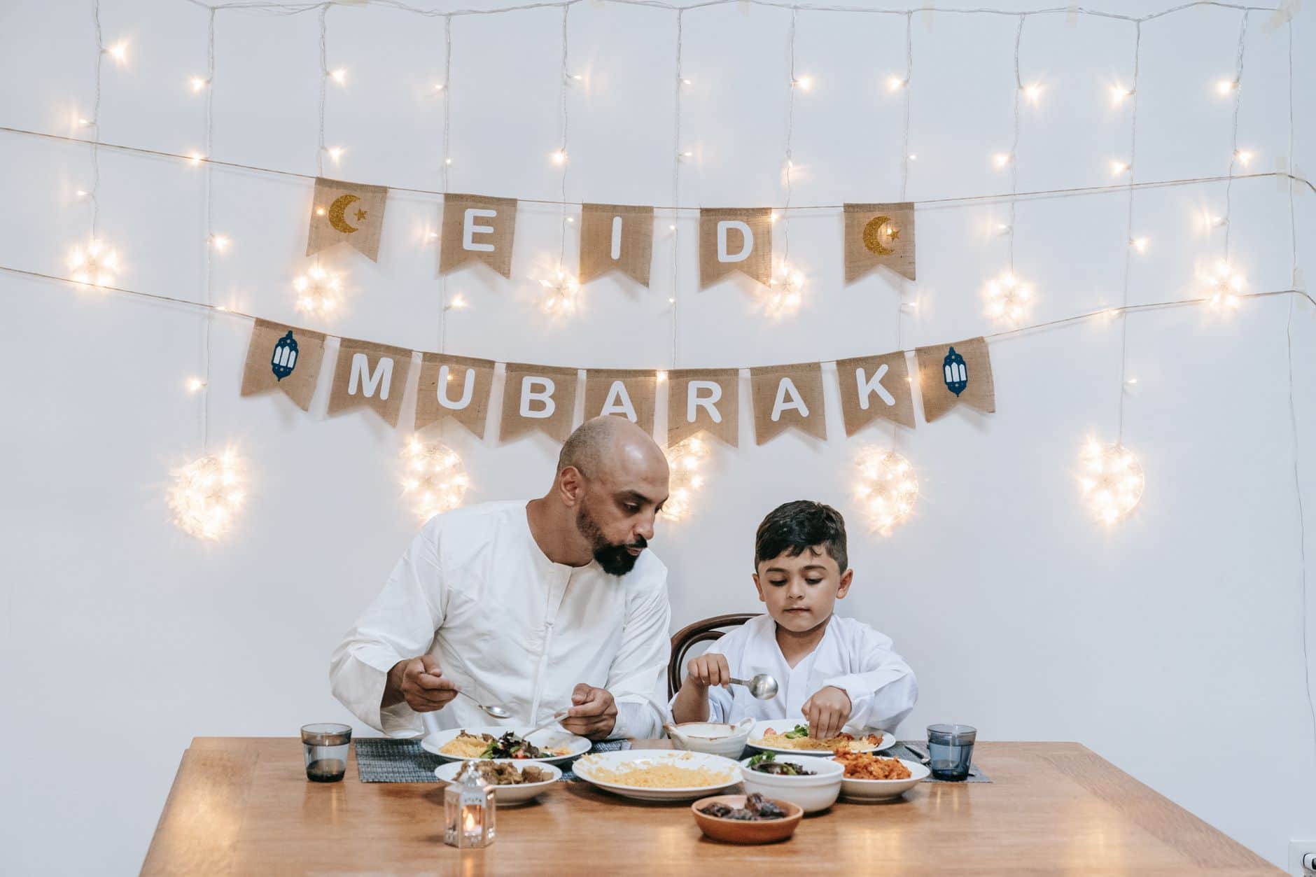 A father and son enjoy a meal together during an Eid celebration with festive decor.